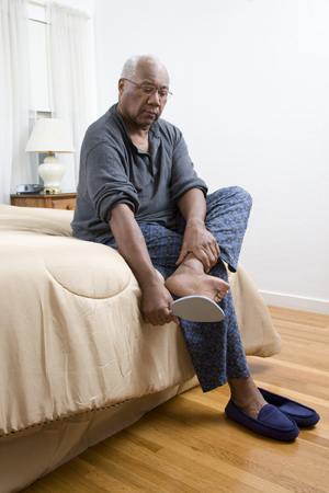 Man sitting on edge of bed looking at sole of foot with mirror.