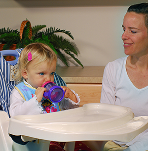 Woman watching toddler girl drink water from sippy cup.