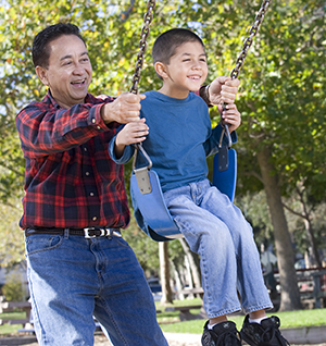 Hombre hamacando a un niño en el columpio de un parque.